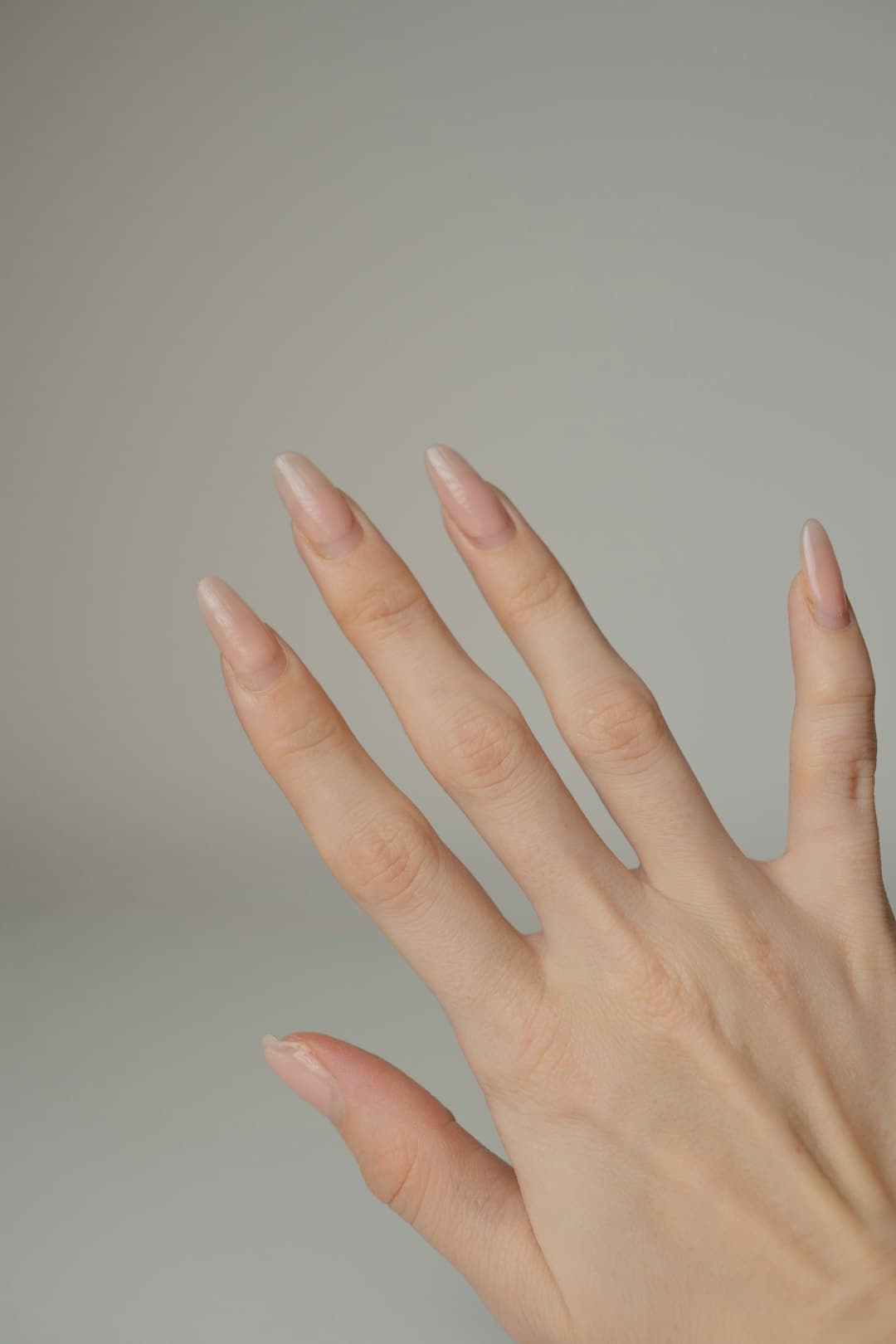 Clean almond nude nails photographed on grey seamless.