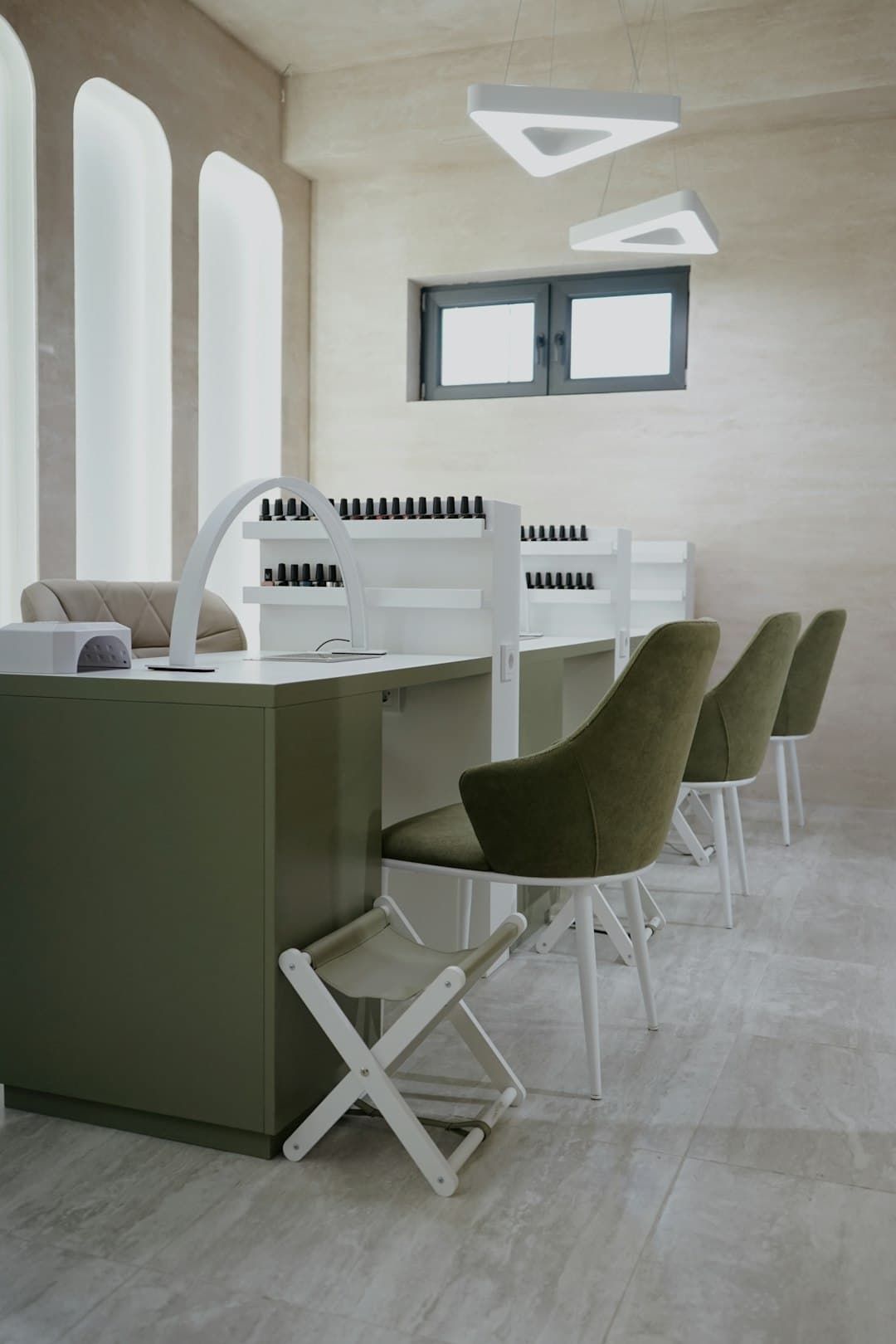Halcyon's two-room studio: warm microcement walls, backlit arched alcoves, sage chairs and lacquer bottles racked on shelves.