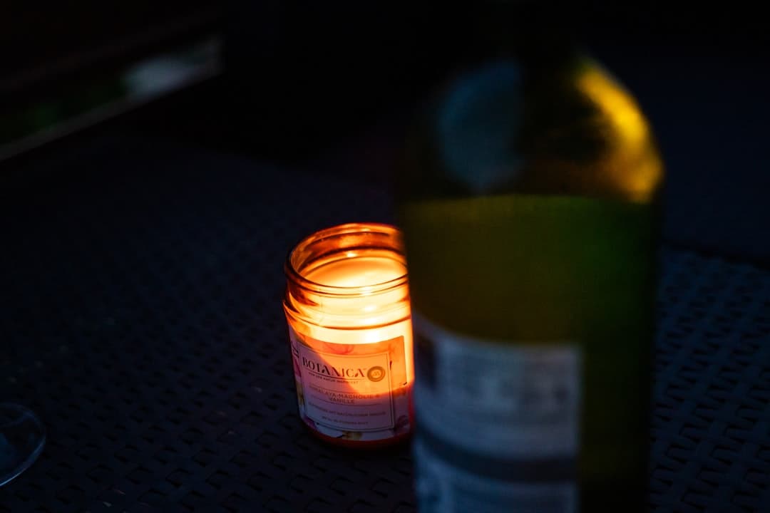 A lit candle beside a wine bottle on the table, the room gone to candlelight.